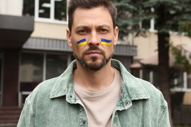 Photo of Man with drawings of Ukrainian flag on face outdoors