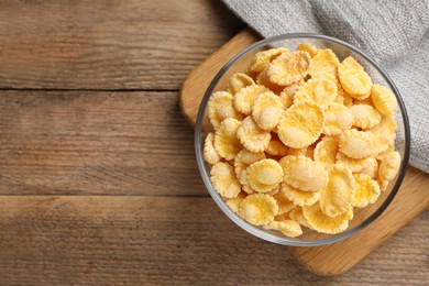Photo of Bowl of tasty corn flakes on wooden table, top view. Space for text