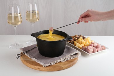 Photo of Dipping piece of ham into fondue pot with tasty melted cheese at white table, closeup