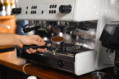 Photo of Barista holding portafilter with milled coffee near machine in bar, closeup. Space for text