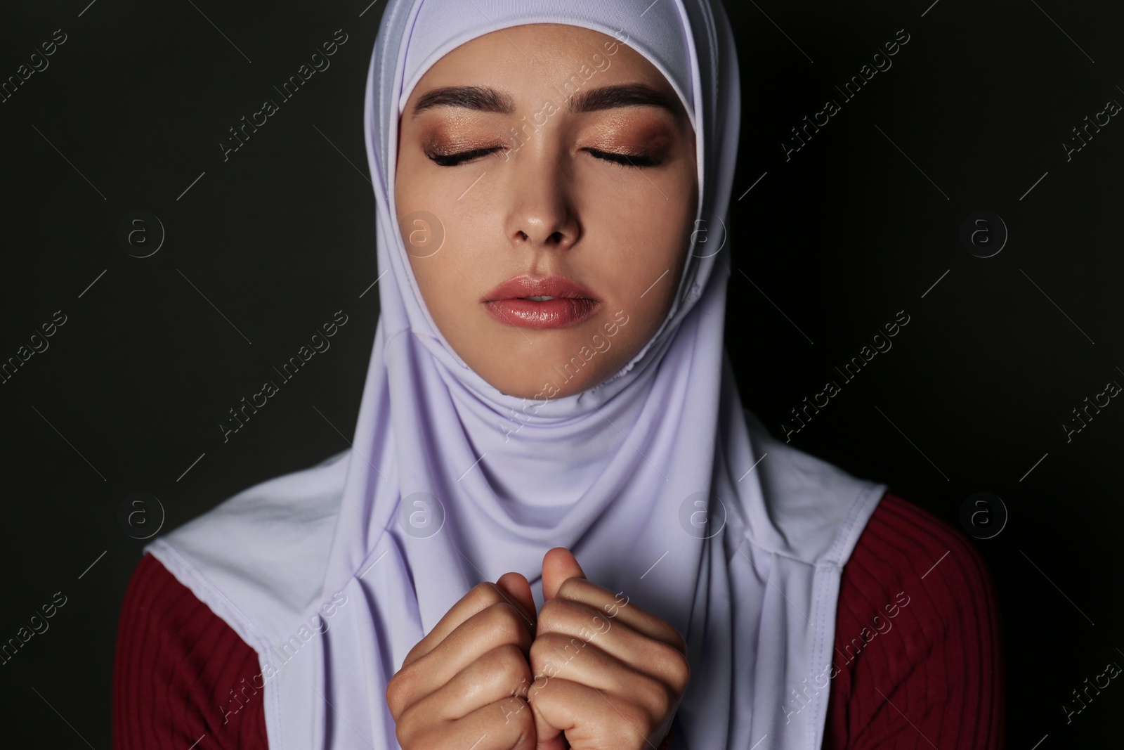 Photo of Portrait of Muslim woman in hijab  praying on dark background