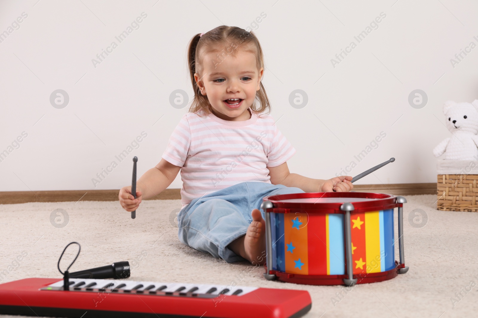 Photo of Cute little girl playing with drum, drumsticks and toy piano at home