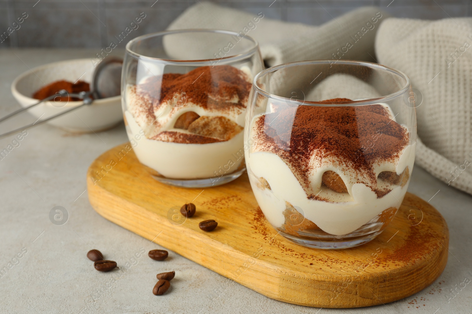 Photo of Delicious tiramisu in glasses and scattered coffee beans on light table