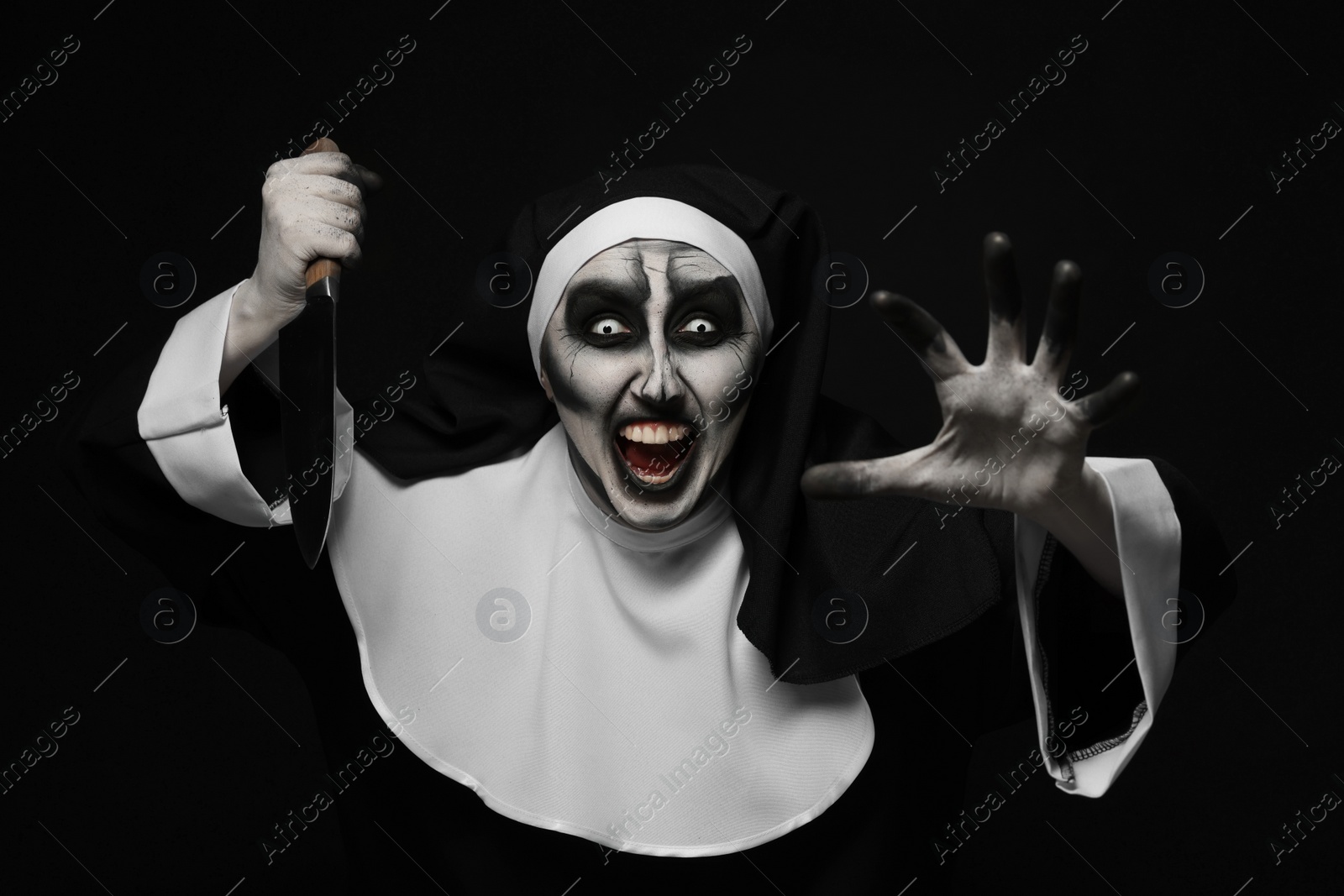 Photo of Scary devilish nun with knife on black background. Halloween party look