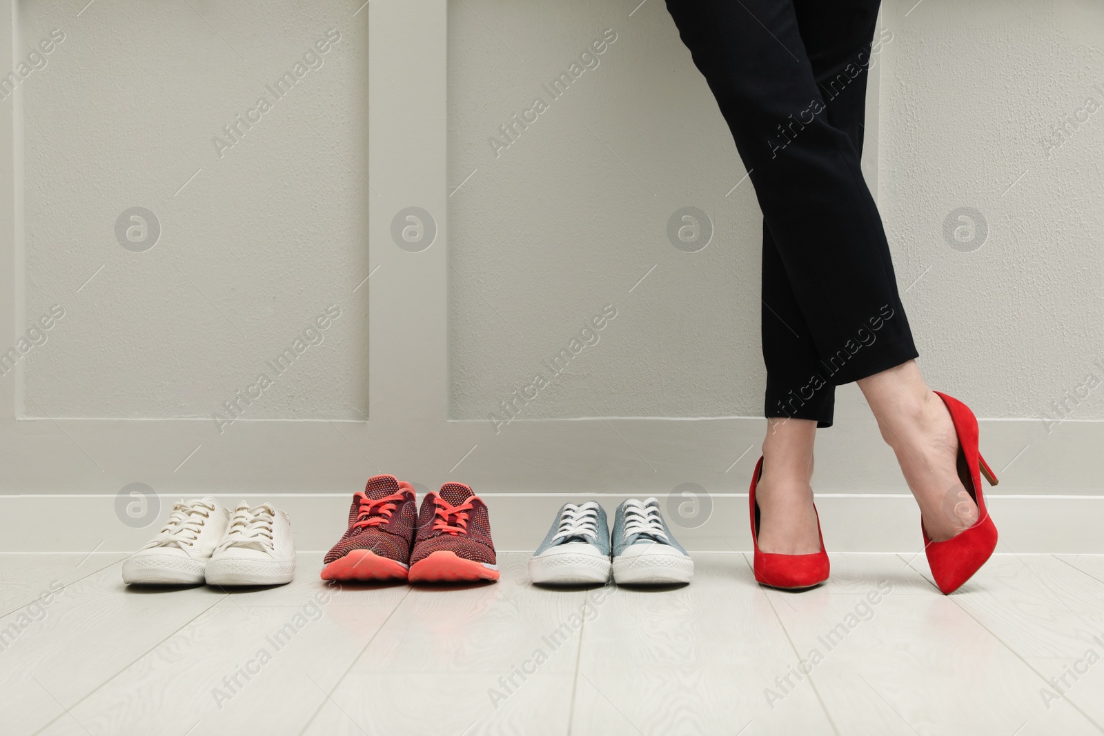 Photo of Businesswoman in high heel shoes standing near different comfortable sneakers indoors, closeup