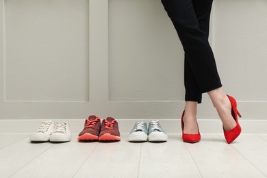 Photo of Businesswoman in high heel shoes standing near different comfortable sneakers indoors, closeup