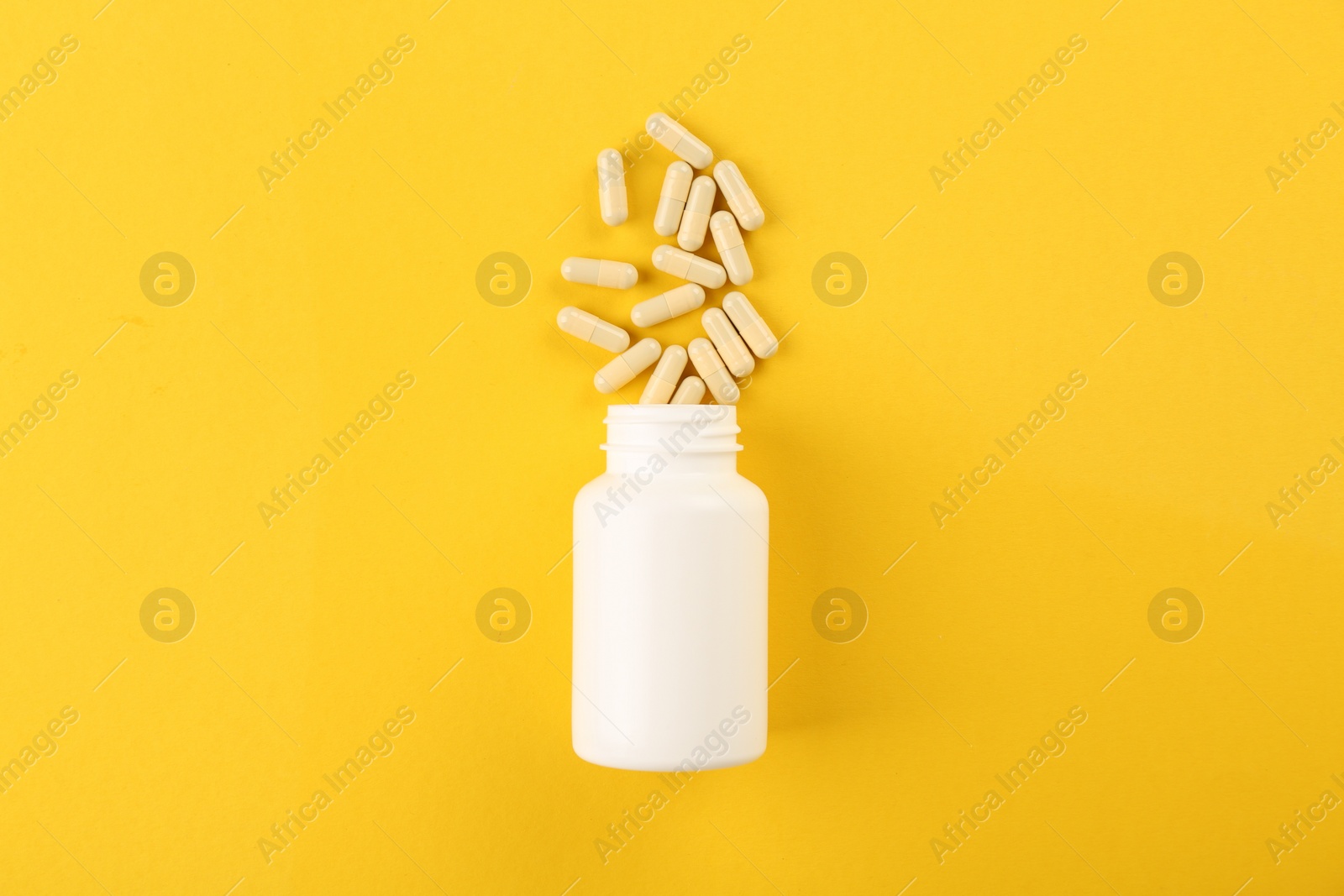 Photo of Bottle and vitamin capsules on yellow background, top view