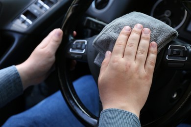 Photo of Man cleaning steering wheel with rag in car, closeup