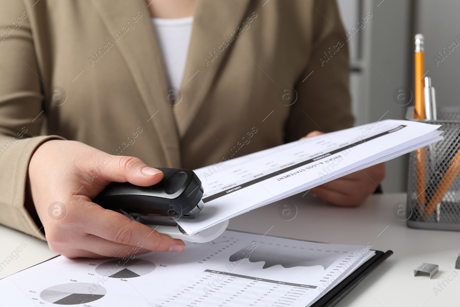 Photo of Woman with documents using stapler at white table indoors, closeup