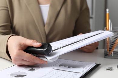 Photo of Woman with documents using stapler at white table indoors, closeup