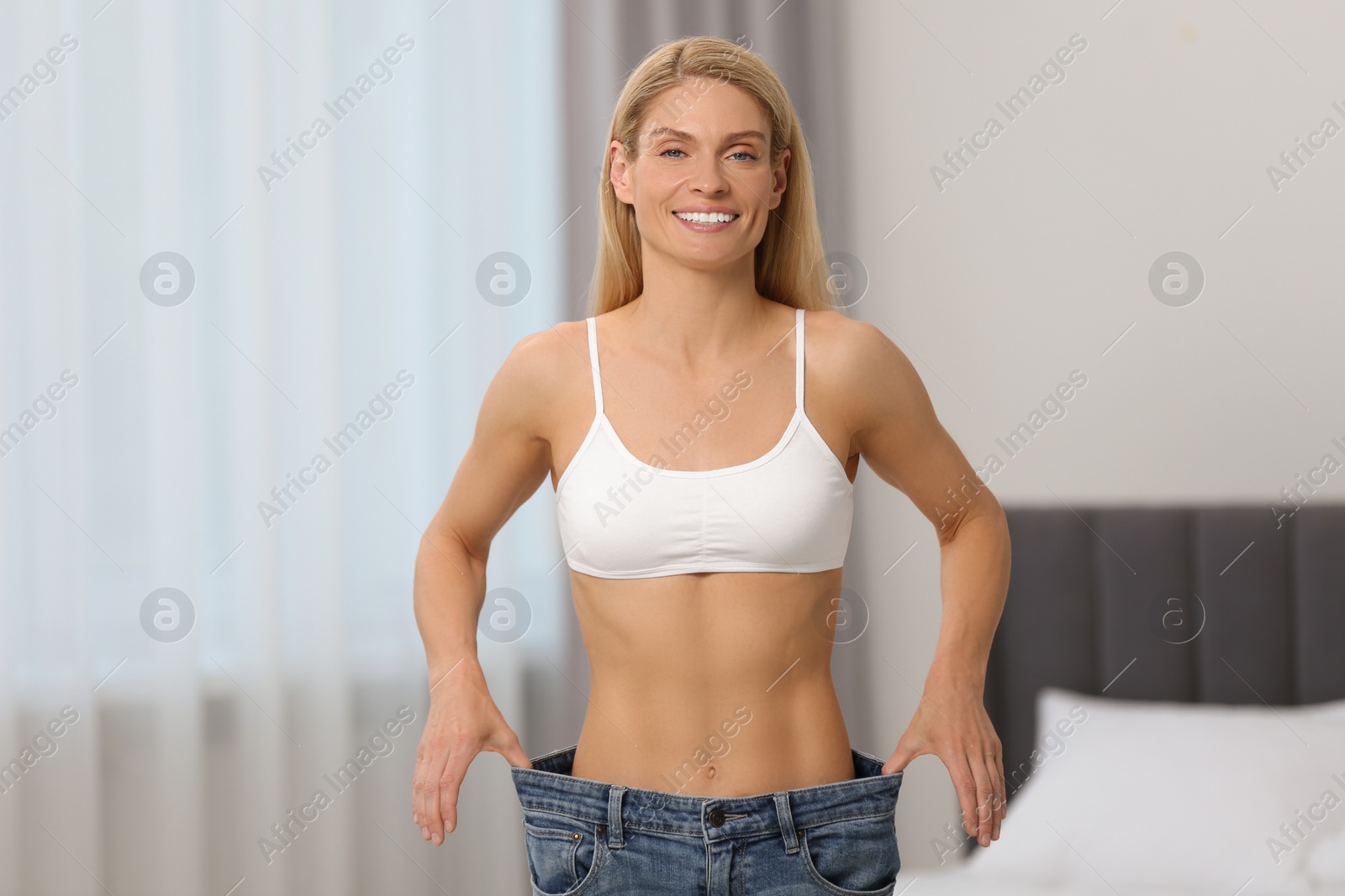 Photo of Slim woman wearing big jeans at home. Weight loss