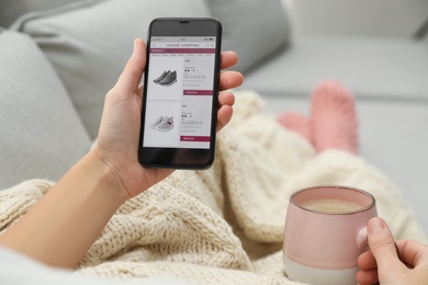 Woman with cup of coffee using smartphone for online shopping indoors, closeup