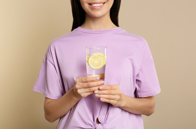 Photo of Woman with tasty lemon water on beige background, closeup