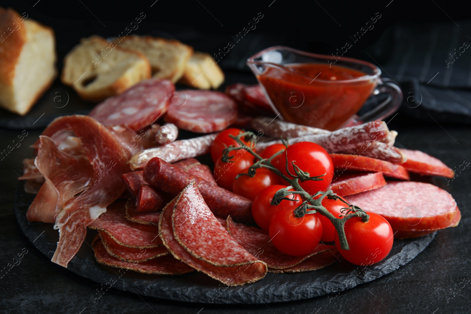 Photo of Different types of sausages with tomatoes served on black table, closeup