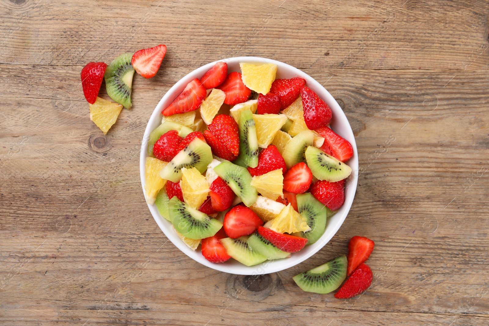 Photo of Delicious fresh fruit salad in bowl and ingredients on wooden table, flat lay