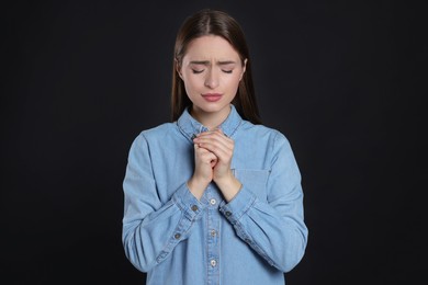 Woman with clasped hands praying on black background