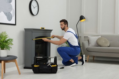 Photo of Professional technician with measuring tape installing electric fireplace in room