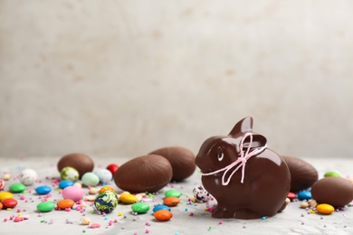 Photo of Chocolate Easter bunny, candies and eggs on light grey table. Space for text
