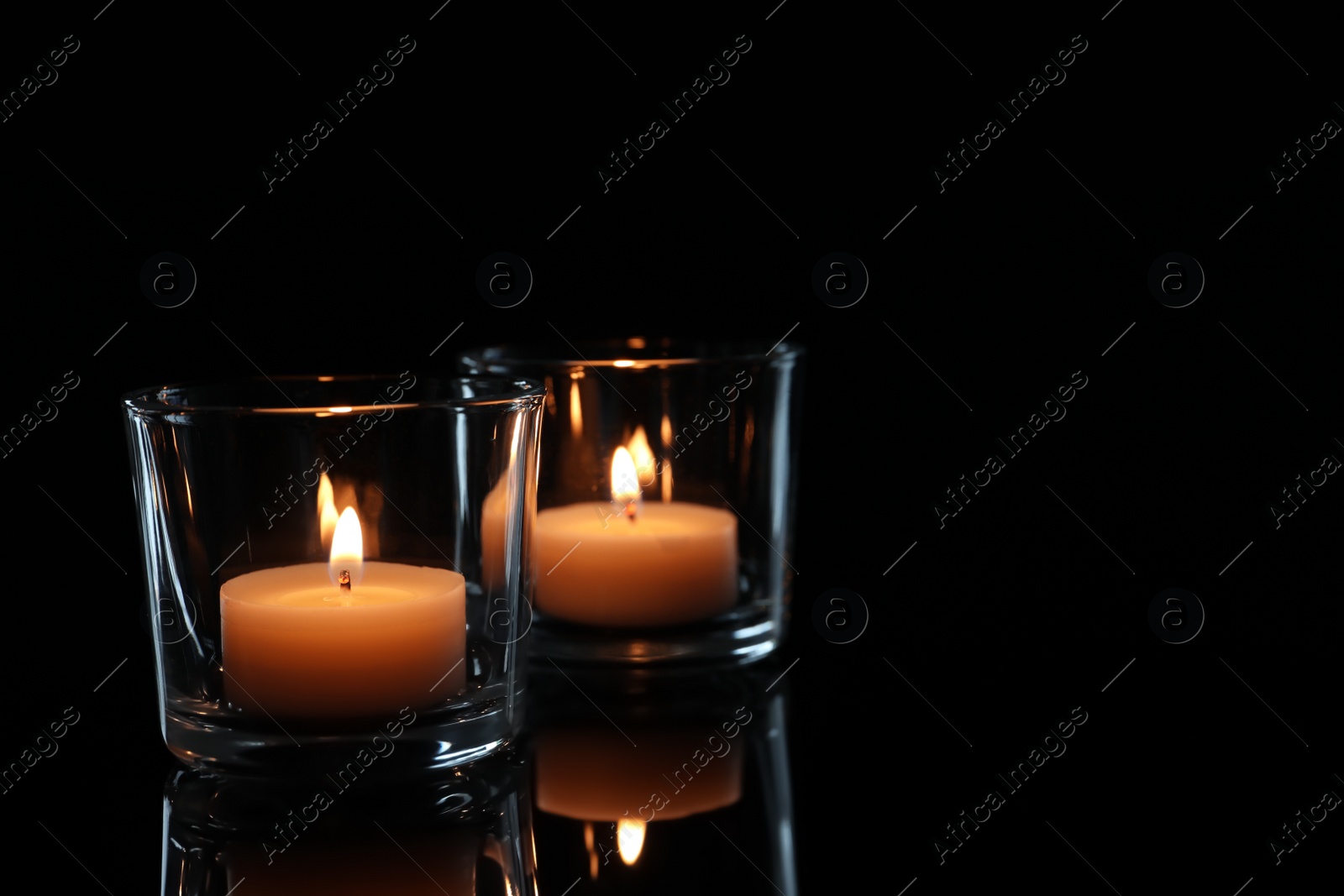 Photo of Wax candles in glasses burning on dark background