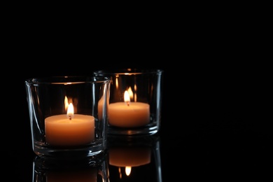 Photo of Wax candles in glasses burning on dark background