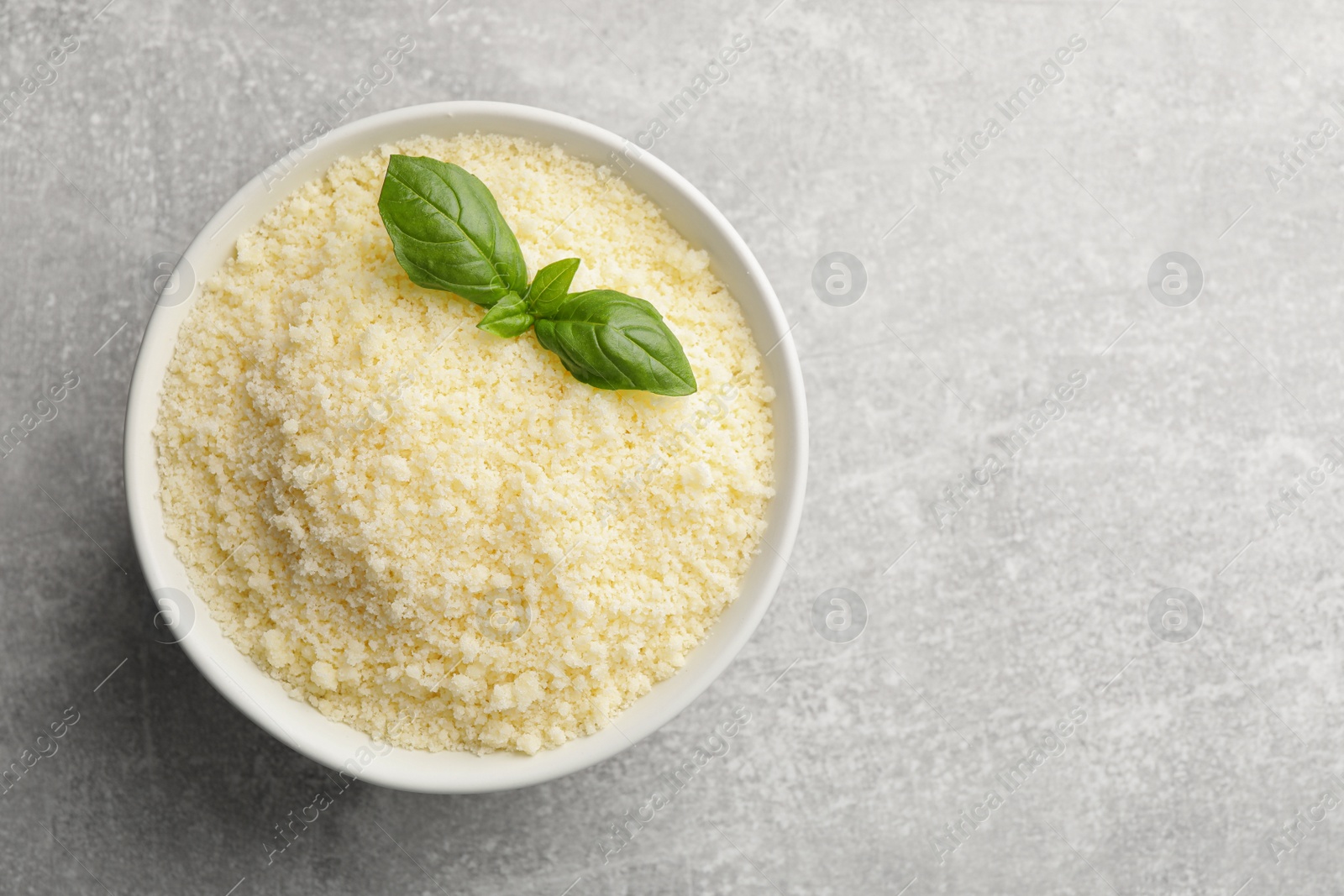 Photo of Bowl with grated parmesan cheese and basil on grey table, top view. Space for text