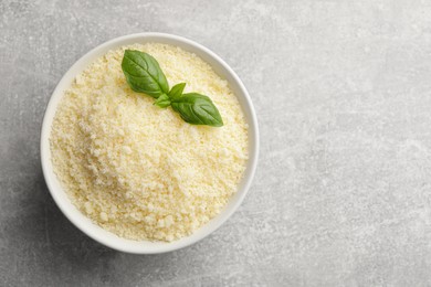 Bowl with grated parmesan cheese and basil on grey table, top view. Space for text