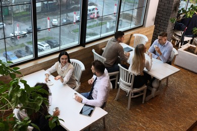 Coworkers having coffee break near window in cafe, above view