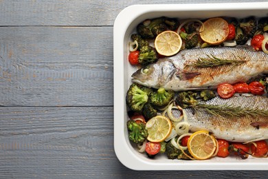 Photo of Delicious fish with vegetables and lemon in baking dish on grey wooden table, top view. Space for text