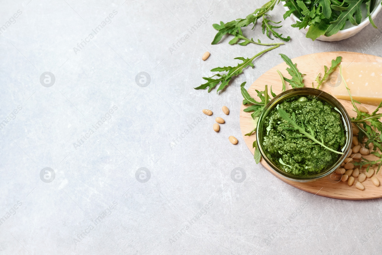 Photo of Bowl of tasty arugula pesto and ingredients on light table, flat lay. Space for text