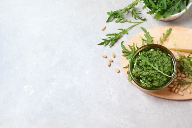 Photo of Bowl of tasty arugula pesto and ingredients on light table, flat lay. Space for text