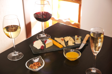 Different delicious cheeses with snacks and glasses of wine on table