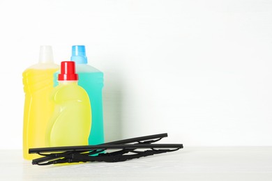 Photo of Bottles of windshield washer fluids and wipers on white wooden table. Space for text