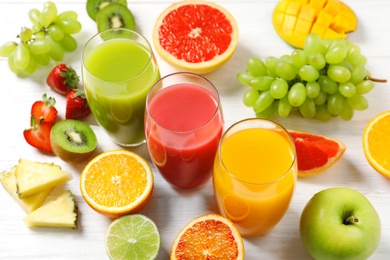 Photo of Glasses with different juices and fresh fruits on wooden table