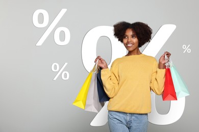 Discount offer. Happy woman with paper shopping bags on light grey background. Illustrations of percent signs behind her