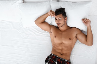 Sexy young man lying on bed with soft pillows at home, top view