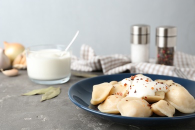 Delicious cooked dumplings with sour cream on grey table. Space for text