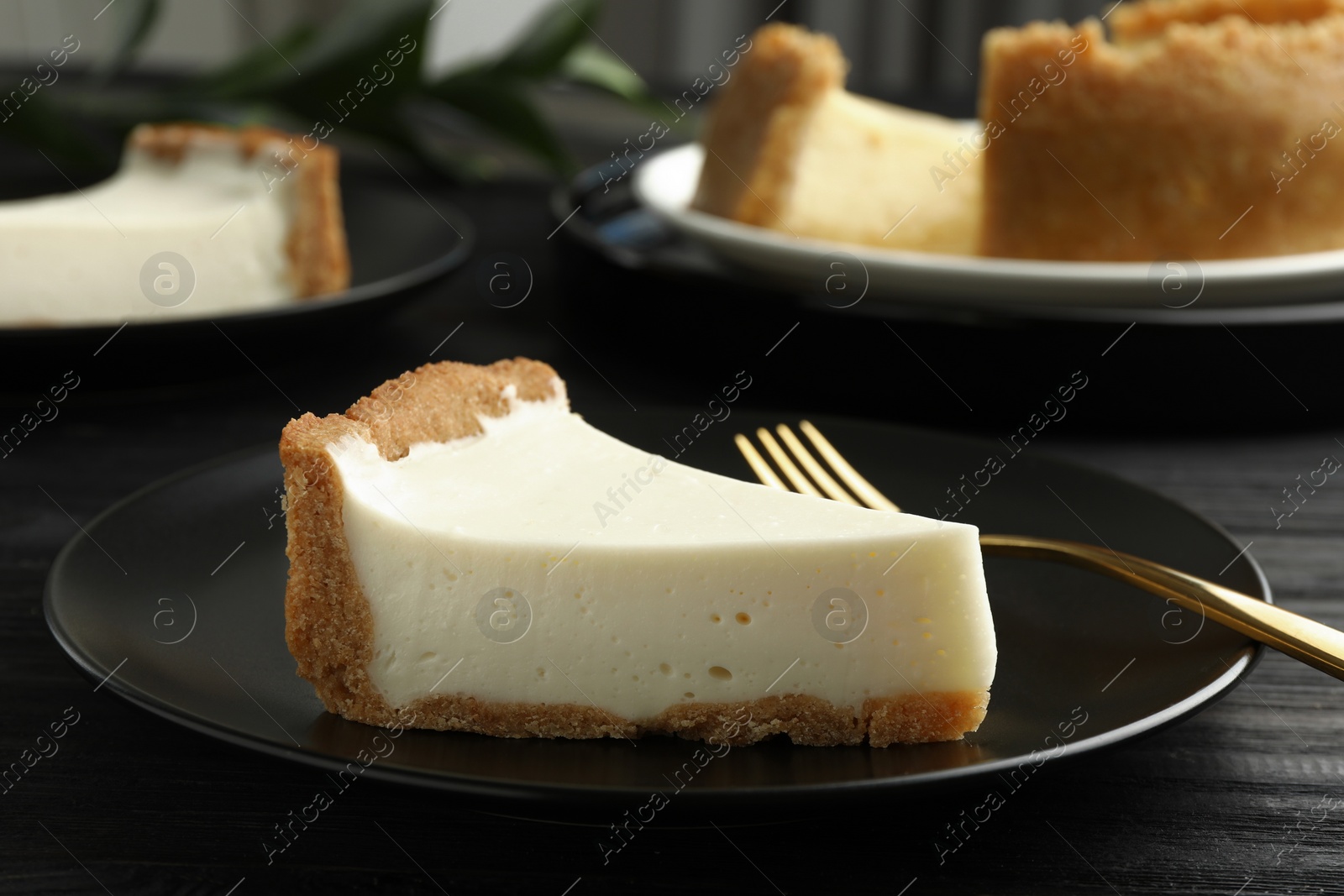 Photo of Piece of tasty vegan tofu cheesecake and fork on black wooden table, closeup