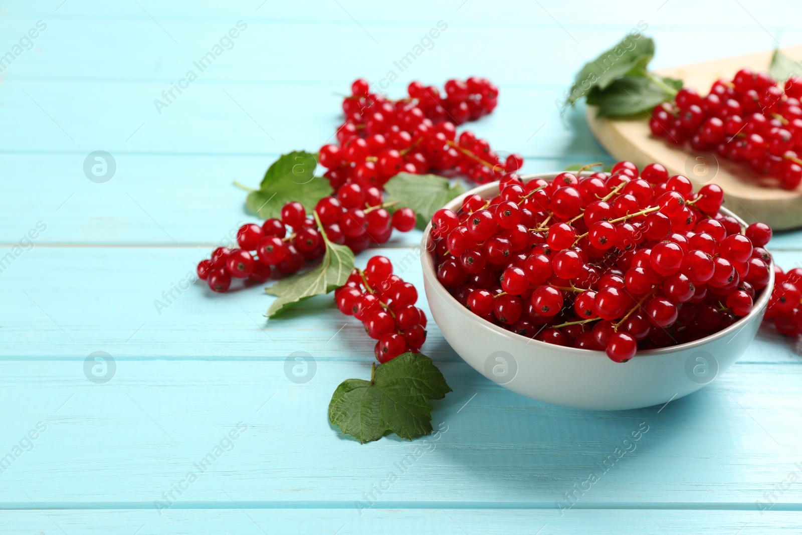 Photo of Delicious red currants and leaves on light blue table