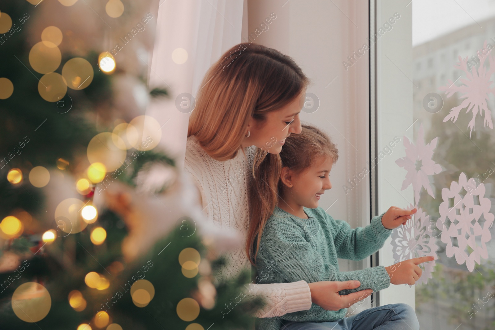 Photo of Happy mother and daughter decorating window with paper snowflakes indoors