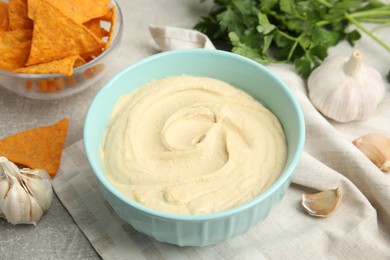 Photo of Delicious hummus, nachos and parsley on grey table, closeup