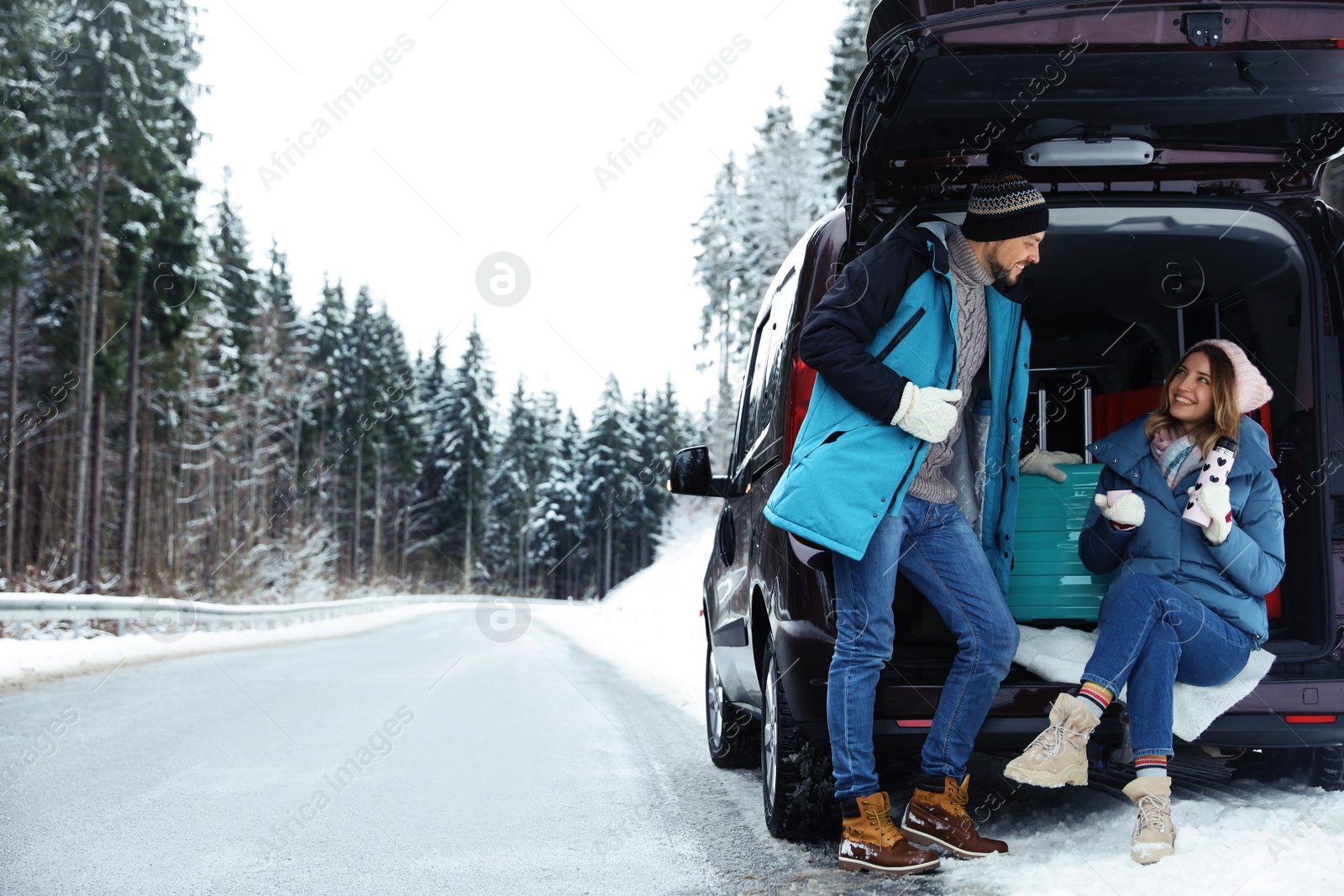 Photo of Couple near open car trunk full of luggage on snowy road, space for text