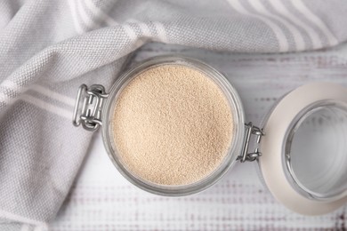 Photo of Granulated yeast in glass jar on white wooden table, top view