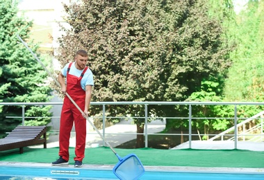 Photo of Male worker cleaning outdoor pool with scoop net