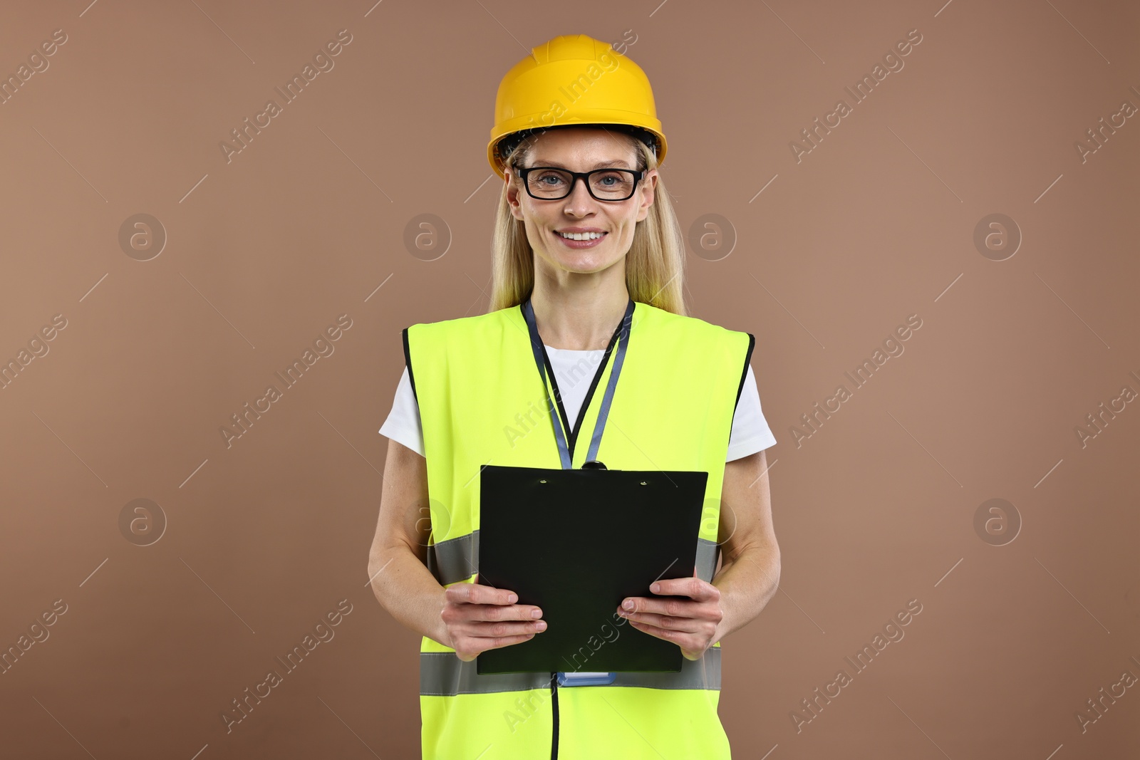 Photo of Engineer in hard hat holding clipboard on brown background