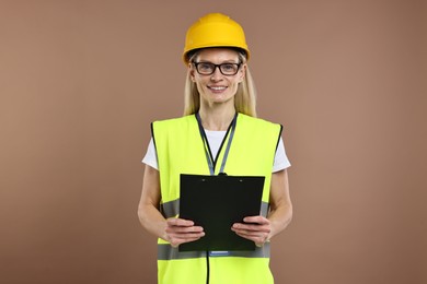 Engineer in hard hat holding clipboard on brown background