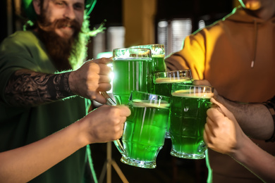 Group of friends toasting with green beer in pub, closeup. St. Patrick's Day celebration