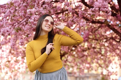 Beautiful woman in sunglasses near blossoming tree on spring day, space for text