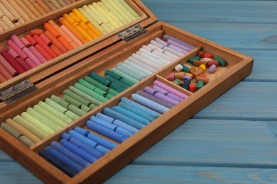 Photo of Drawing pastel set in box on light blue wooden table, closeup