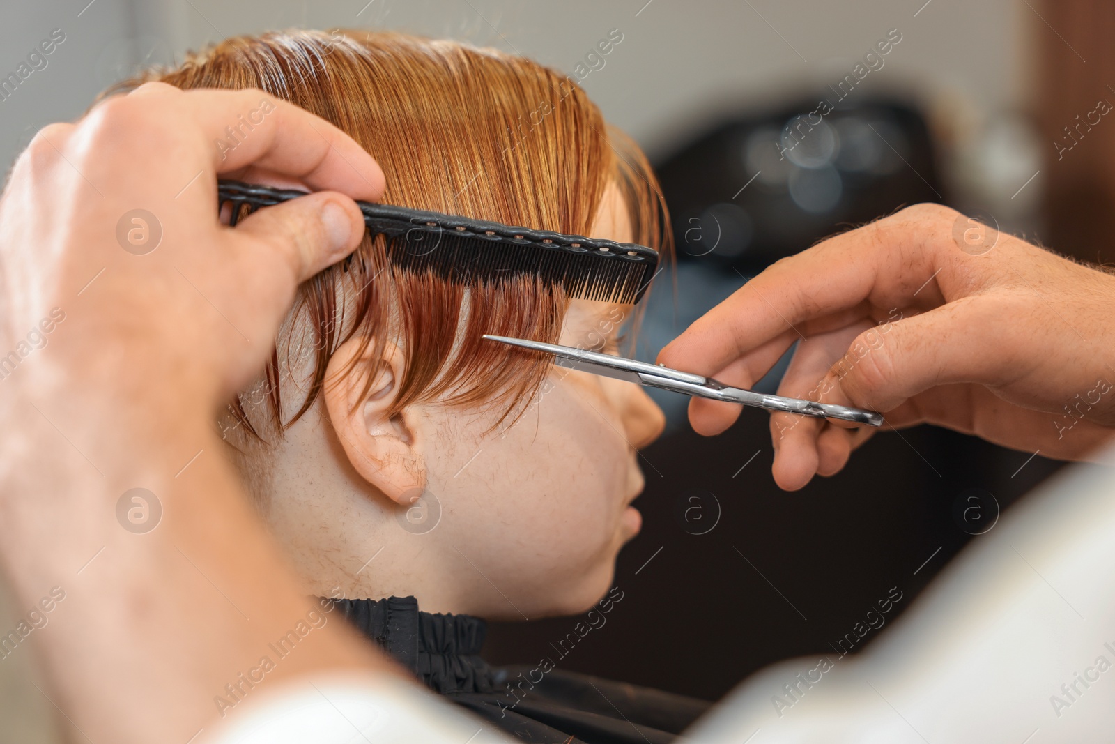 Photo of Professional hairdresser cutting boy's hair in beauty salon, closeup