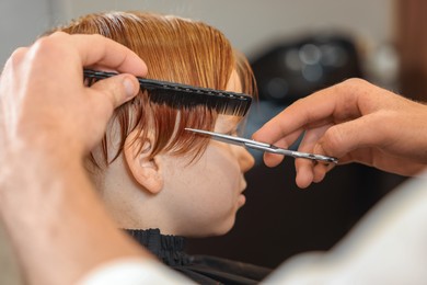 Professional hairdresser cutting boy's hair in beauty salon, closeup